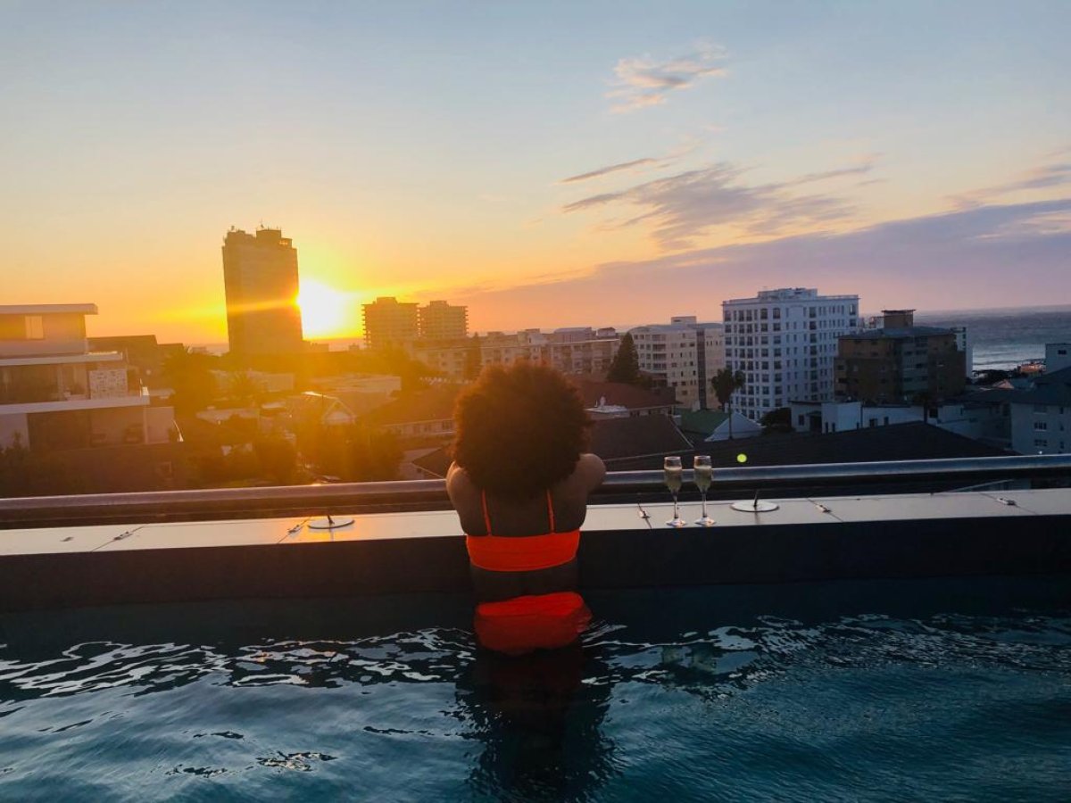 Black woman on a rooftop pool with a sunset