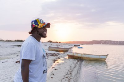 Black man near a lagoon smiling wearing a colourful hat.