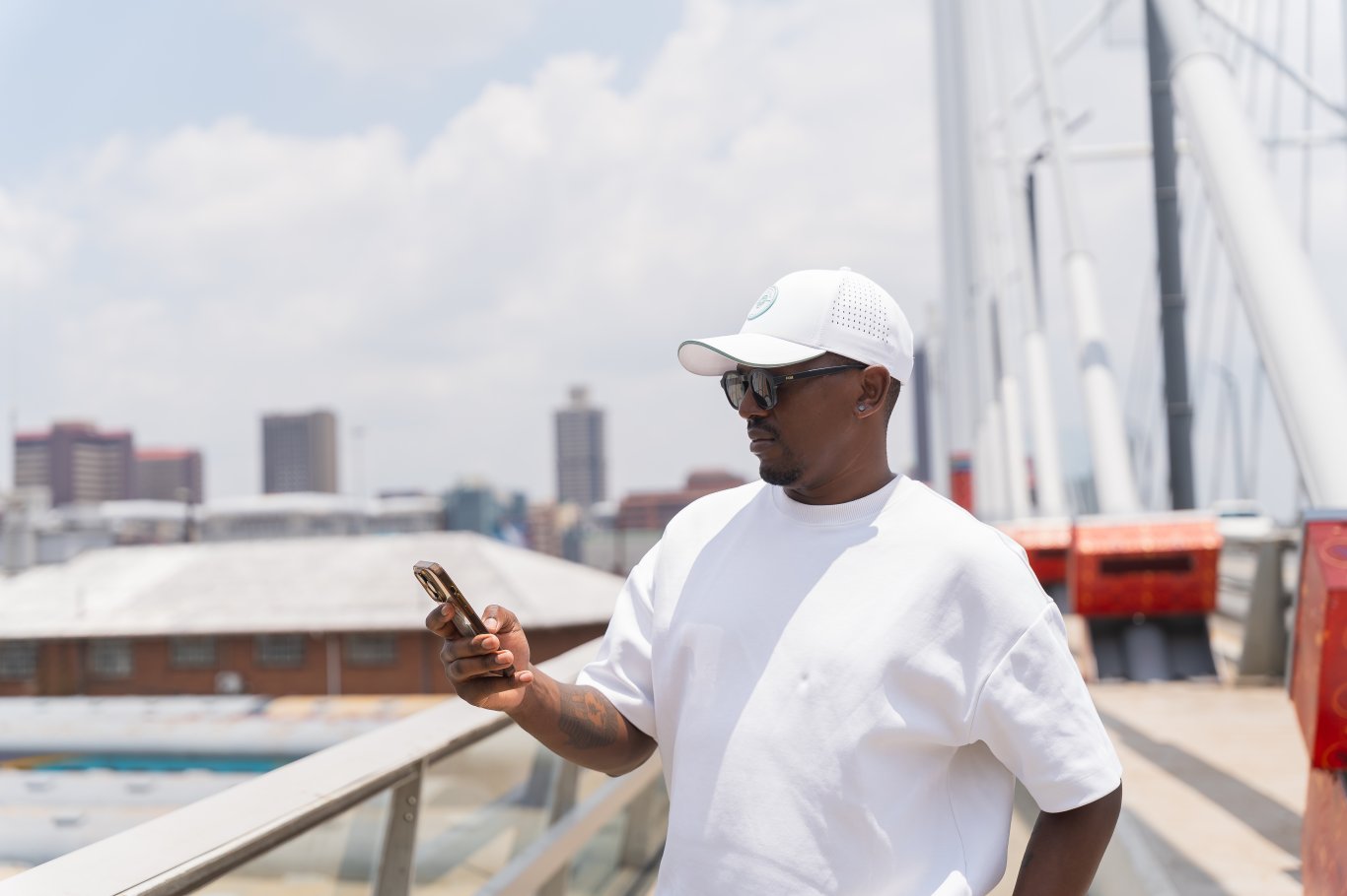 Black man looking at phone wearing sunglasses on Nelson Mandela bridge.