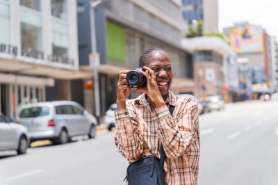 Black woman photographer smiling in the streets with a camera looking away