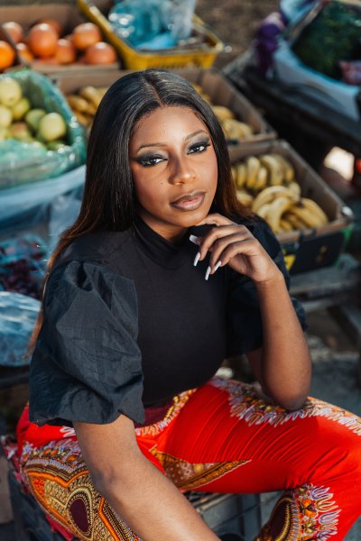 African woman sitting near fruits and vegetables outside wearing pattern pants
