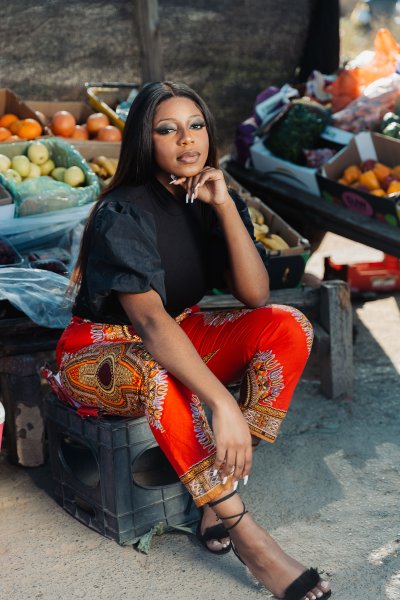 african woman sitting near fruits and vegetables outside wearing pattern pants