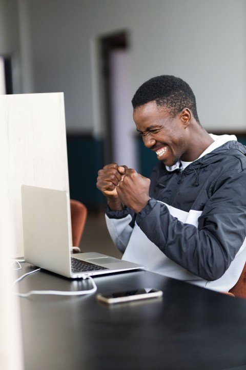 Black man celebrating a win and looking at his laptop with a grin