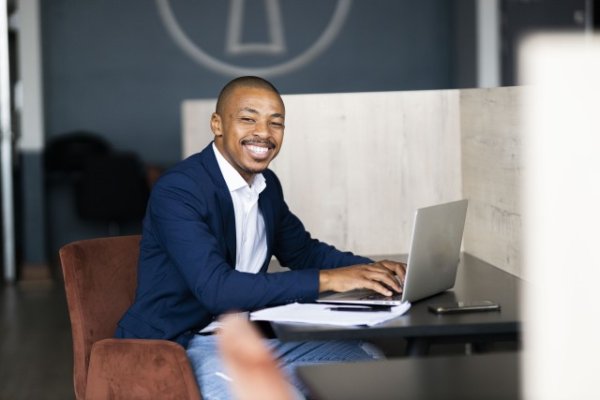 Black business man wearing a suit and looking at the camera while working on his laptop