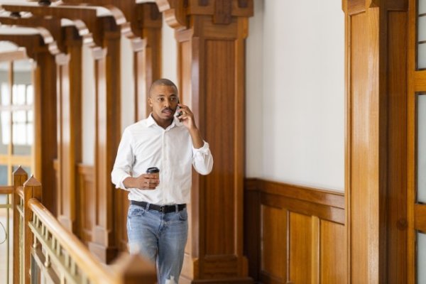 Black business man at work holding coffee and talking on the phone