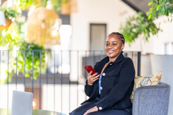 Black corporate woman sitting on the couch in a co working space holding phone.