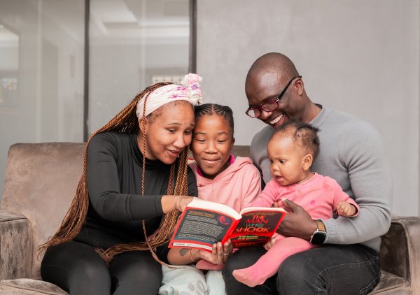 Black family reading a book and smiling on the couch at home.