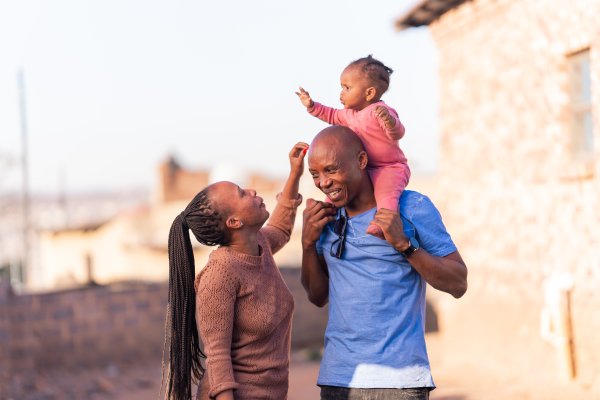 Black family with father and mother playing with daughter wearing pink, sunny day.