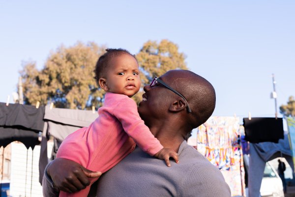 Black father and daughter outdoors smiling with clothes and blue sky in the background.