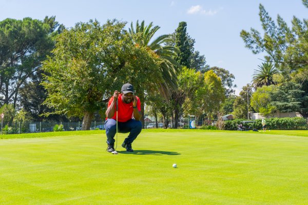 Black male golfer wearing a red golf shirt on the golf course putting