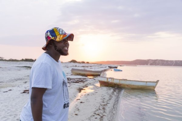 Black man near a lagoon smiling wearing a colourful hat.
