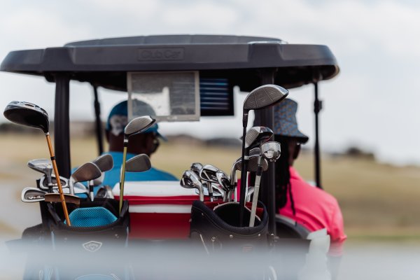 Golf clubs in the back of a golf cart with two black male golfers