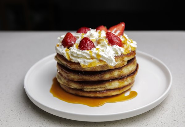 Well made pancakes with strawberries and cream on a white plate.