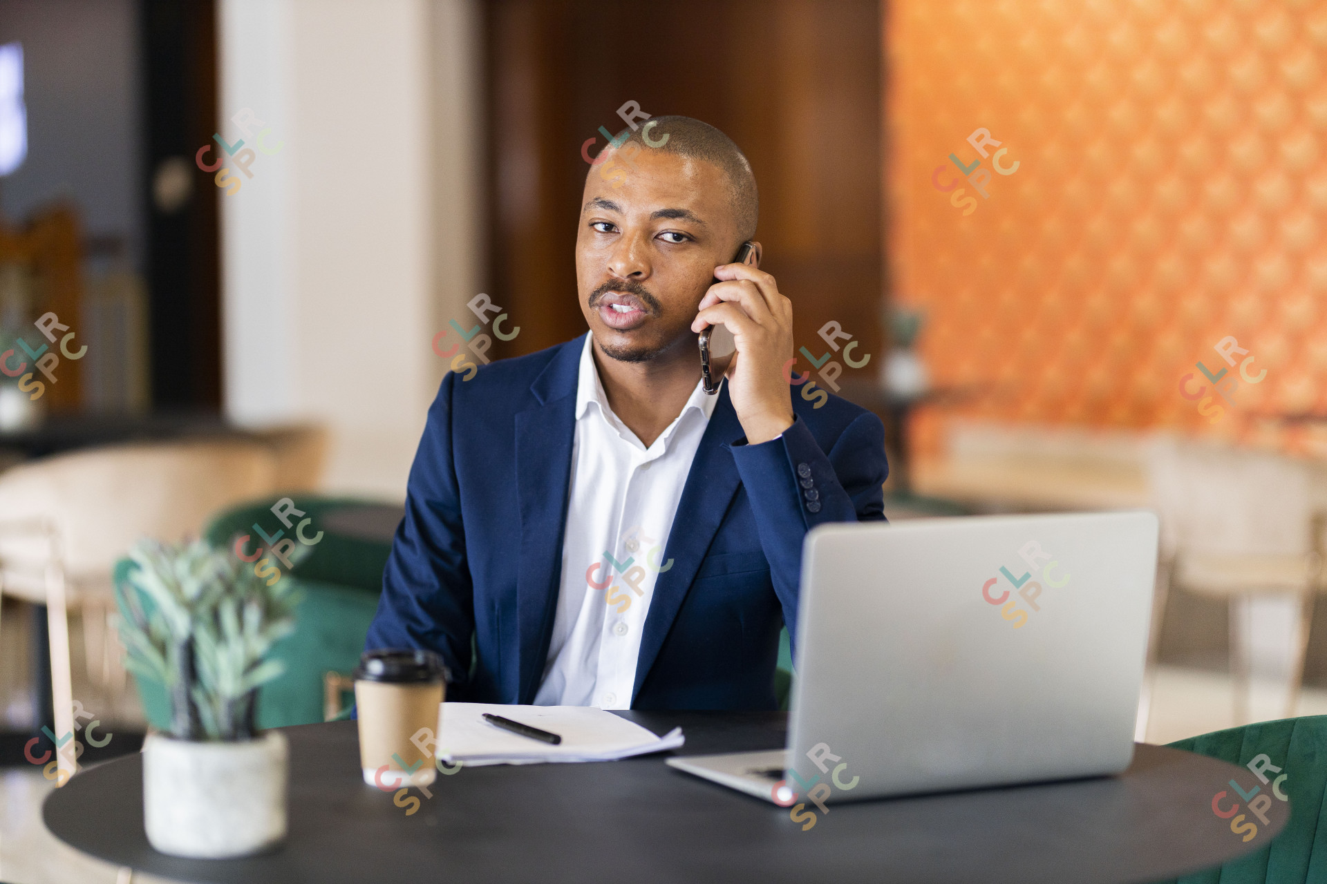 Black business man on a phone call and working on his laptop at a coffee shop