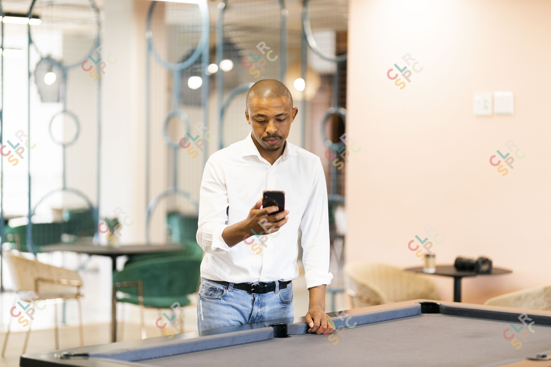 Black man looking at his cellphone by a pool table at work
