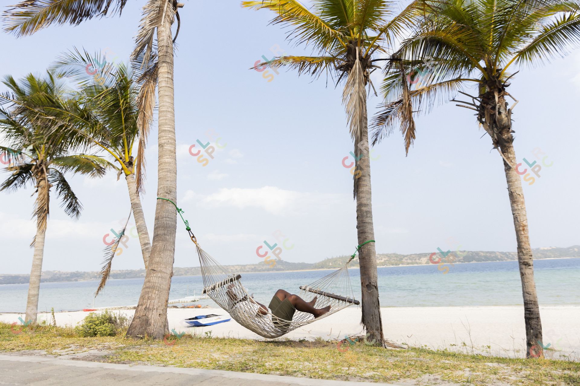 Black man resting on a hammock near a lagoon.