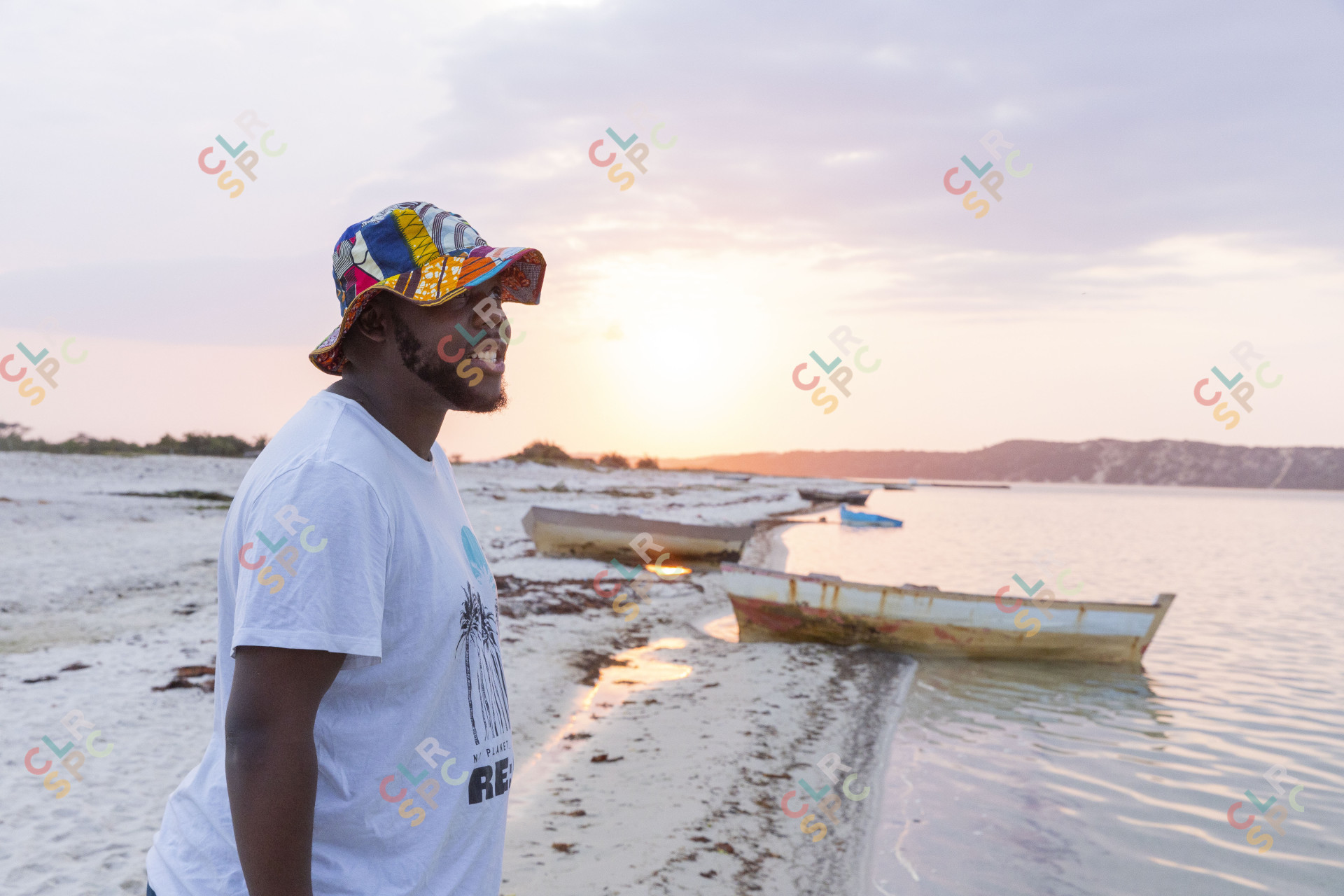 Black man near a lagoon smiling wearing a colourful hat.