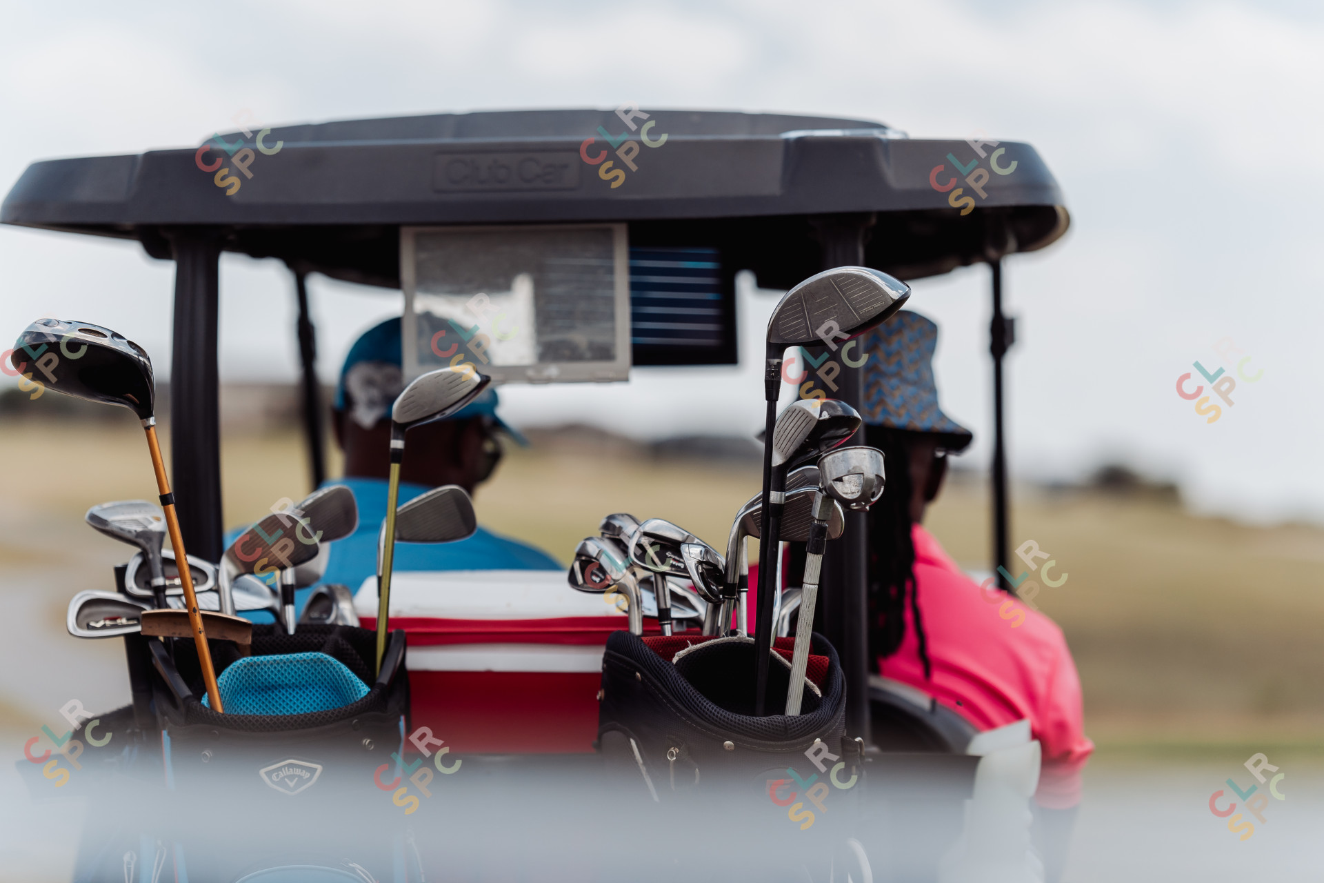 Golf clubs in the back of a golf cart with two black male golfers