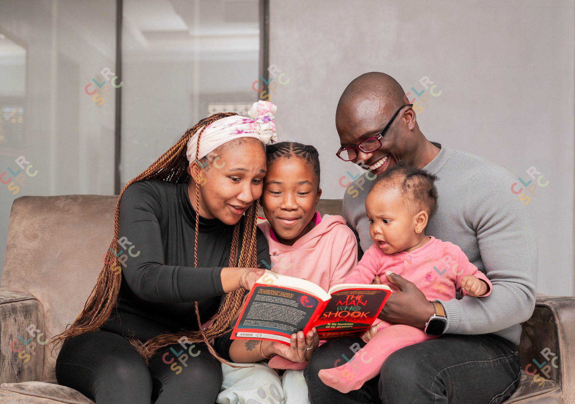 Black family reading a book and smiling on the couch at home.