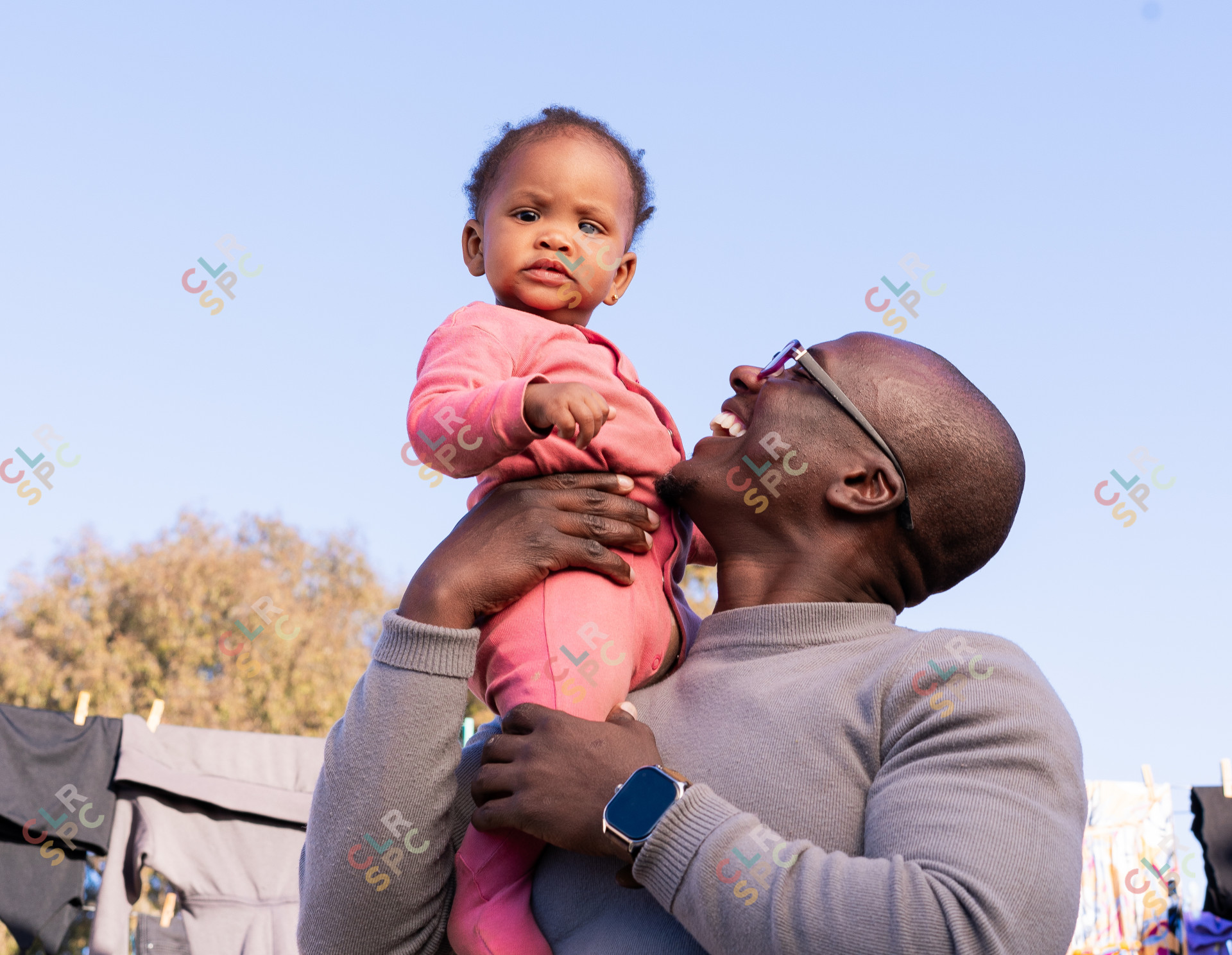 Black father holding daughter and smiling with clothes hanging in the background
