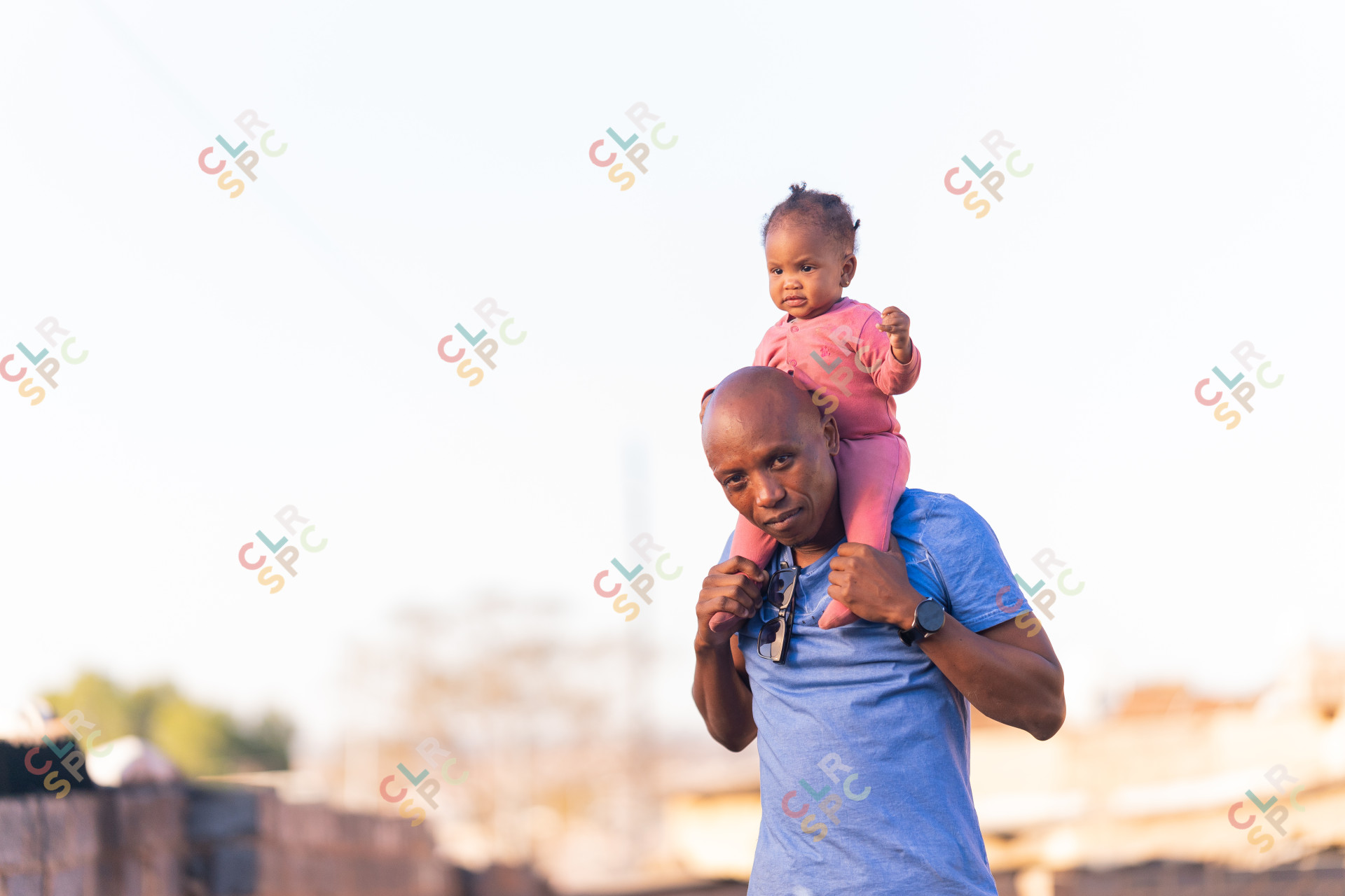 Father and daughter play outside, daughter wearing pink and father wearing a blue shirt on a sunny day.