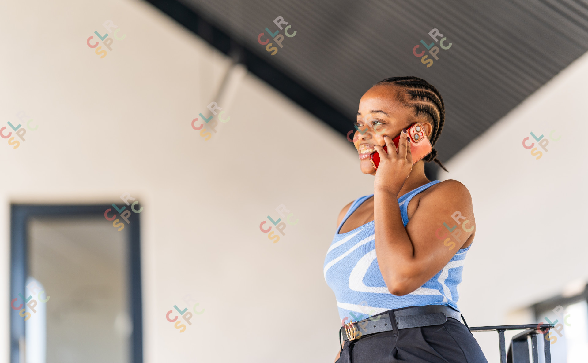 Young black woman on the phone smiling at the office with braids and a blue top.