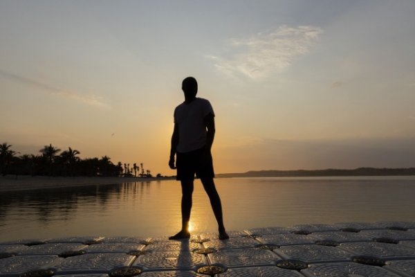 Silhouette of black man near a lagoon of water.