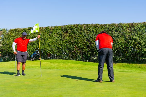 Two black men wearing a red golf shirts putting