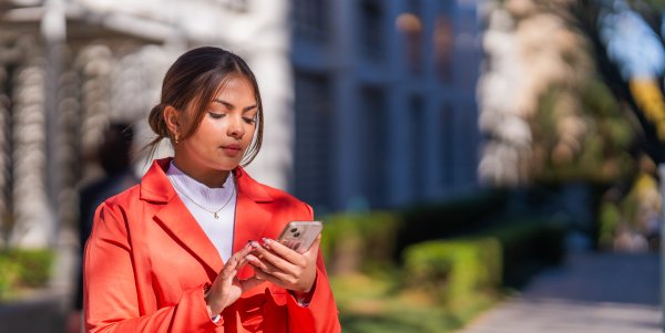 Young mixed race corporate woman holding phone outside.